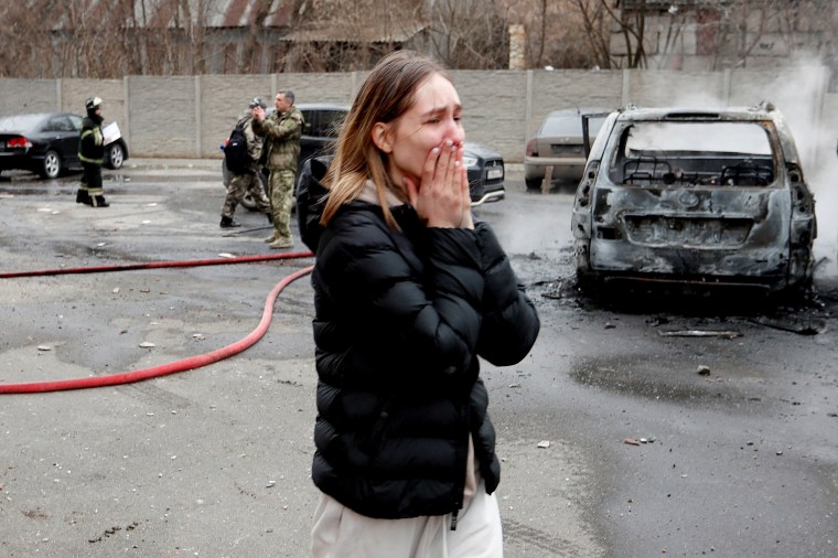 Image: A woman reacts next to a damaged residential building in Donetsk