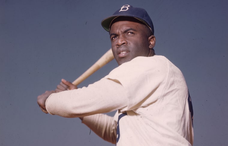 Image: A portrait of the Brooklyn Dodgers' Jackie Robinson in uniform, preparing to swing a baseball bat.