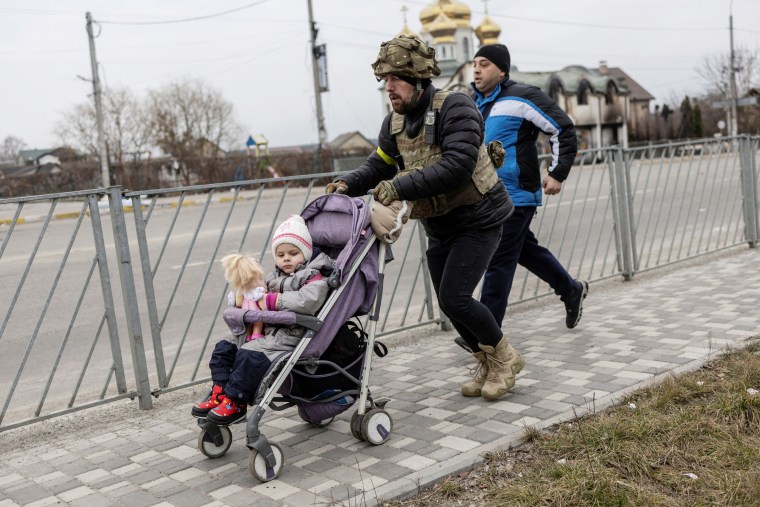 Image: A service member of the Ukrainian armed forces helps to evacuate a child from the town of Irpin, on the only escape route used by locals after days of heavy shelling, while Russian troops advance towards the capital, in Irpin, near Kyiv