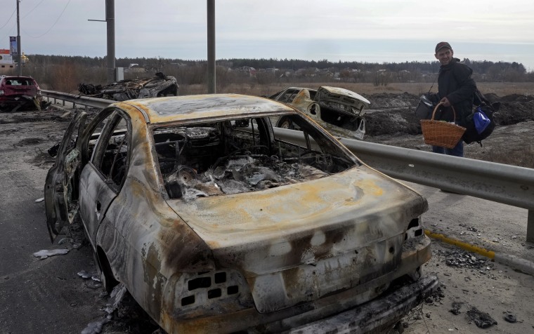 A resident passes by cars burnt in the Russian shellfire as he flees on Saturday, March 12, 2022, from his hometown on the road towards Kyiv, in the town of Irpin.