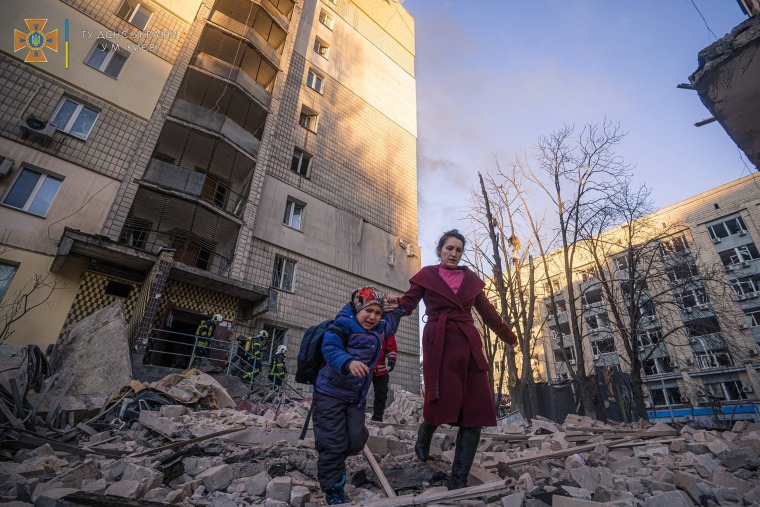 Image: A woman with a child evacuates from a residential building damaged by shelling in Kyiv