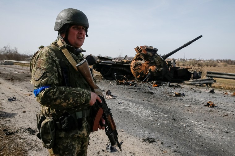 A Ukrainian soldier stands near the wreck of a Russian tank on the front line in the Kyiv region on March 28, 2022.