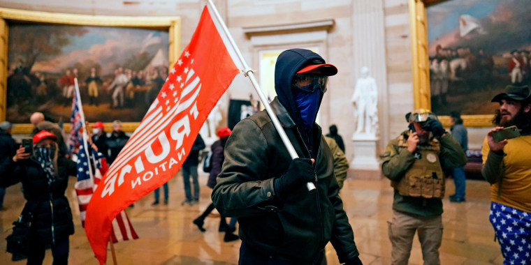 Image: A protestor holding a red flag that reads,\"Trump\" inside the Capitol in Washington, D.C.