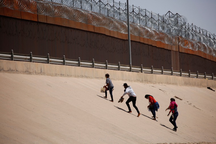 Asylum-seeking migrants walk near the border wall in El Paso, Texas, after crossing the Rio Grande