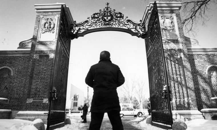 Image: A guard looking up at the gate to Harvard Yard at Harvard University.