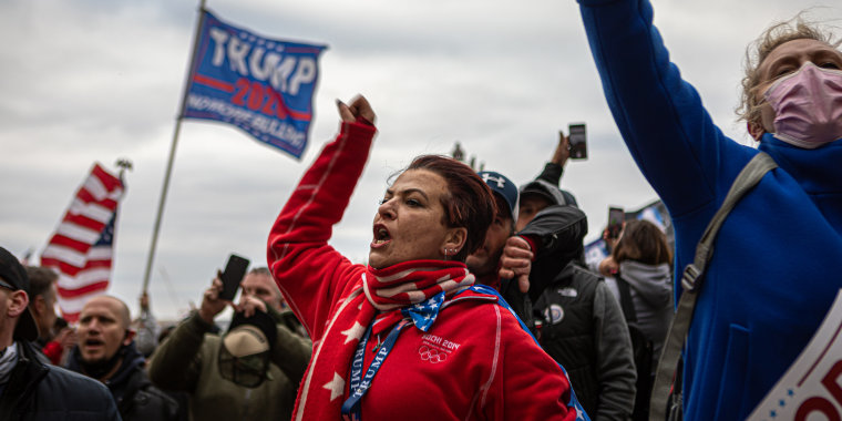 Image: A woman shouting amidst protesters waving the American flag and a flag that reads,\" Trump 2020\".