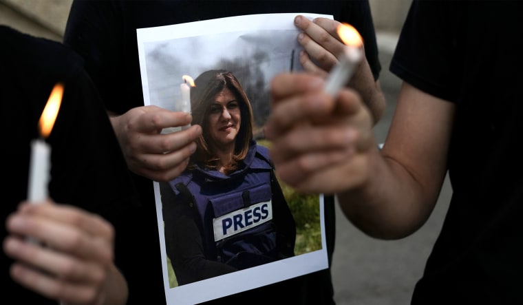 Image: Close up of hands holding candles and a photo of Shireen Abu Akleh