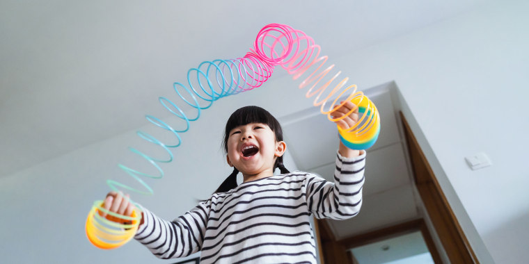 Low angle shot of a joyful little Asian girl playing with a colourful magic spring rainbow toy at home. Simple joy and happiness. Learning through play concept