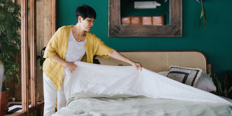 Senior Asian woman doing her morning routine, making up her bed at home