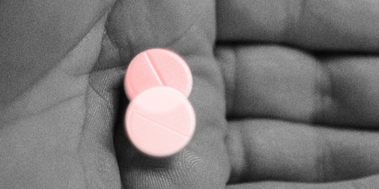 Photo illustration: A hand holding holding two pills with a light pink color overlay.