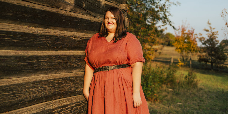 Beautiful and sexy plus size woman in linen red dress standing near wooden wall outdoors at the countryside