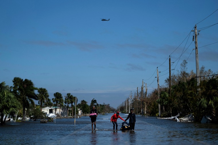 Image: People carrying belongings wade through a flooded neighborhood in Fort Myers, Fla., after Hurricane Ian on Sept. 29, 2022.