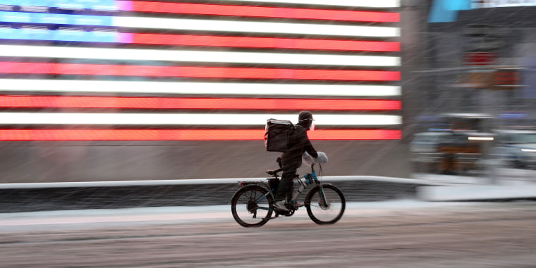 Image: A food delivery guy on a bicycle is seen as snowfall blankets the Times Square in New York City.