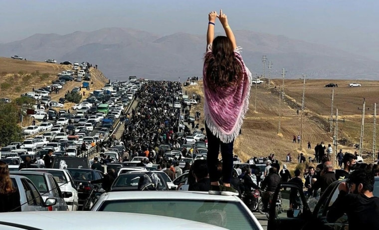 A woman stands on top of a car as protesters make their way toward the cemetery where Mahsa Amini is buried.