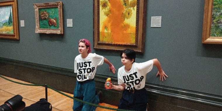 Image: Two protesters wearing t-shirts that read \"Just Stop Oil\" kneeling in front of the  Vincent Van Gogh's 1888 painting 'Sunflowers' after throwing Heinz Tomato soup at it, at the National Gallery in London.