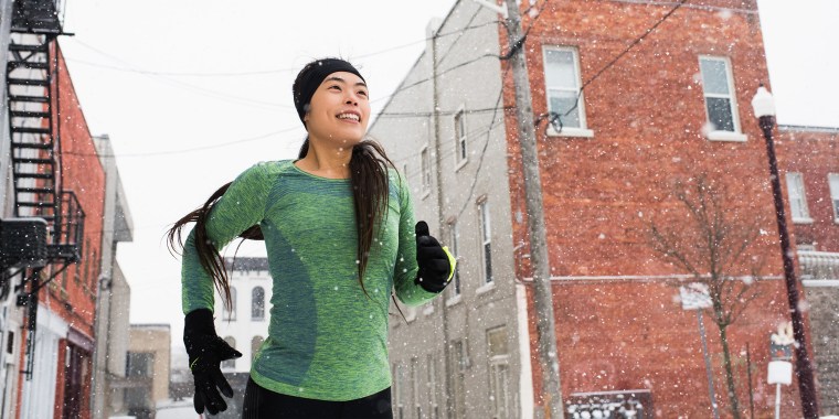Happy young female runner in knit hat running in snowy stree