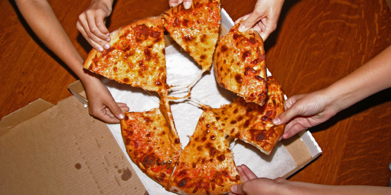 People grabbing slices of pizza, overhead view