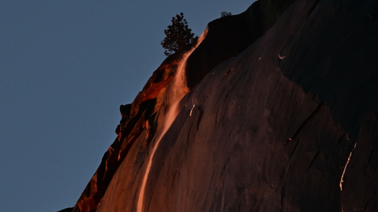 Water flowing off Horsetail Fall glows orange while backlit from the setting sun during the \"Firefall\" phenomenon in Yosemite National Park, California on February 15, 2023.