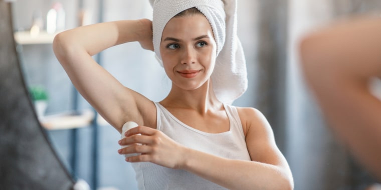 Millennial girl using roller deodorant after shower near mirror at bathroom