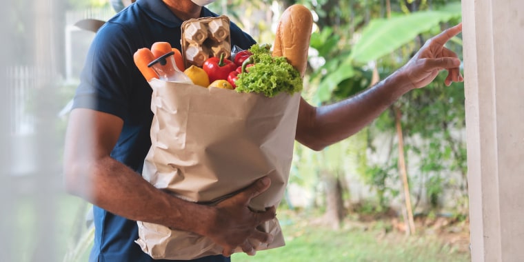 African American delivery man wearing protective face mask holding grocery paper bag of Healthy Food with fresh vegetables, milk, bread