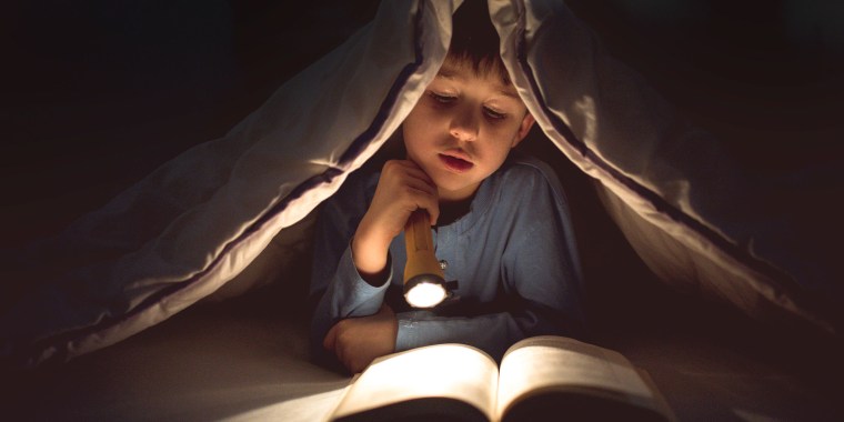 Little boy using a flashlight to read in his bed
