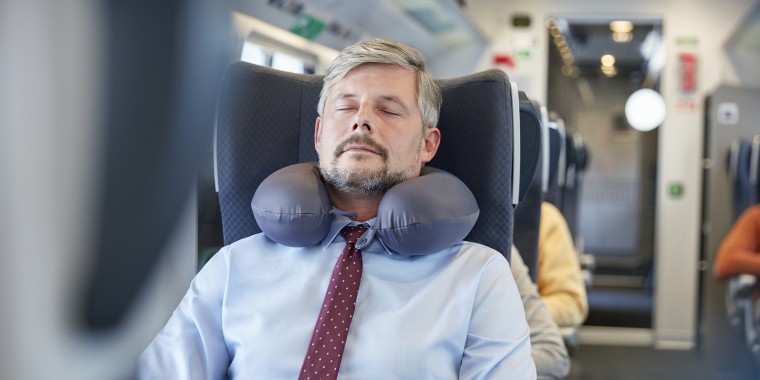 Tired businessman with neck pillow sleeping on passenger train