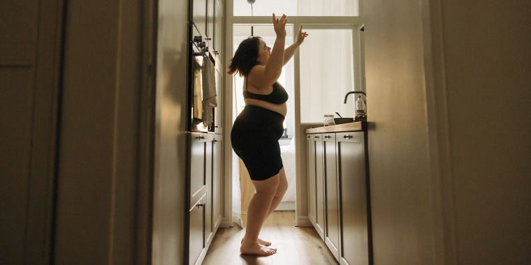 Young voluptuous woman with arms raised enjoying dance in kitchen