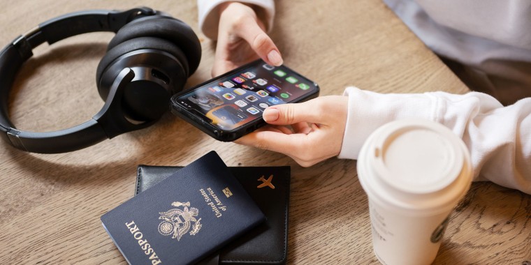 Woman at a coffee shop on her phone, surrounded by her passport and headphones