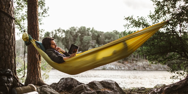 Young man reading book while lying down over hammock in forest