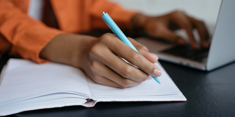 Close-up shot of student hand holding pen and writing in notebook, working at home. E-learning