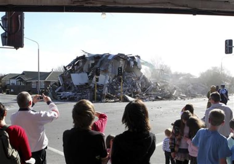 Pedestrians watch as a house damaged from Saturday's earthquake is demolished in Christchurch