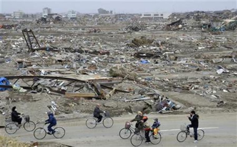 People ride bicycles amidst debris of buildings wrecked by last week's earthquake and tsunami in Natori City