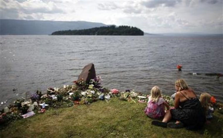 Woman and her daughters sit near flowers left on a memorial on the shore of Tyrifjorden lake