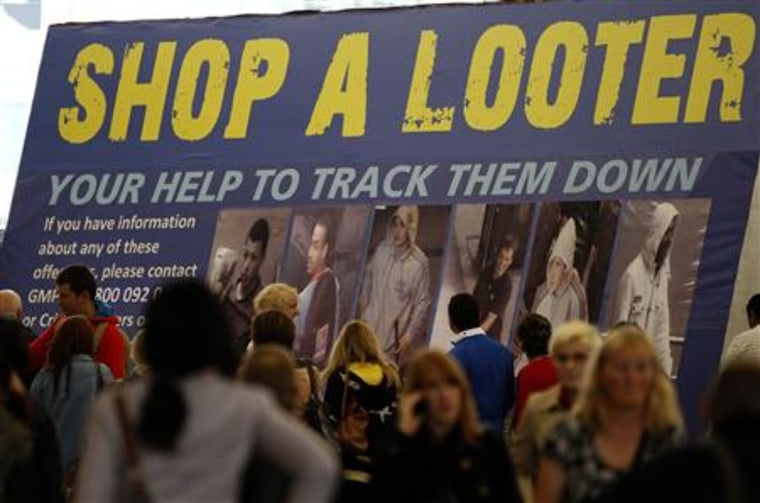 Shoppers walk past a Greater Manchester Police advertising board displaying images of people suspected of committing crimes during the recent riots in Manchester