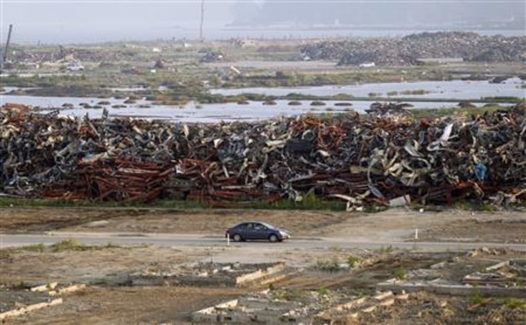 A car drives past piles of wrecked vehicles, destroyed by the March 11th earthquake and tsunami, in Rikuzentakata in this August 14, 2011 file photo.