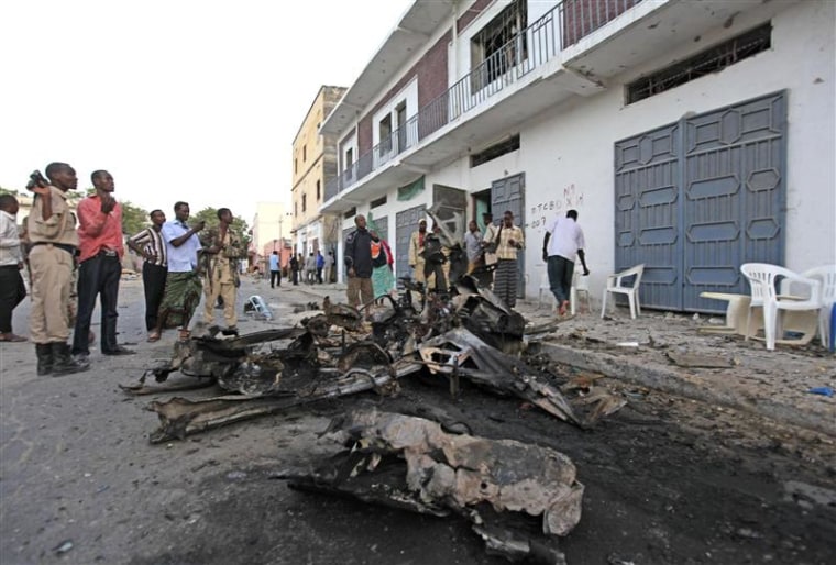 Somali people stand near the scene of a suicide car bomb that exploded leaving scores killed near Muna Hotel in Somalia