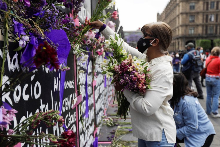A woman places flowers beside the names of victims of femicide in Mexico on fences placed outside the National Palace ahead of a Women's Day protest in Mexico City on March 7, 2021.