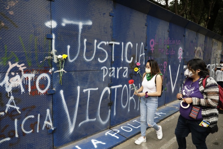 Young women bring flowers to the perimeter wall of the Quintana Roo state offices sprayed with graffiti that reads in Spanish "Justice for Victoria," during a protest in Mexico City on March. 29, 2021.