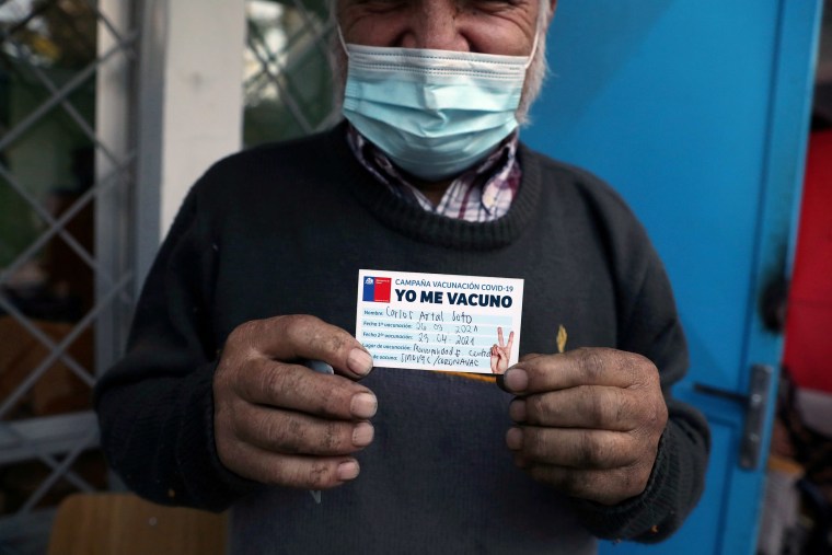 Image: A homeless man shows an ID reading 'I got vaccinated' after receiving a dose of Sinovac's CoronaVac vaccine in Santiago