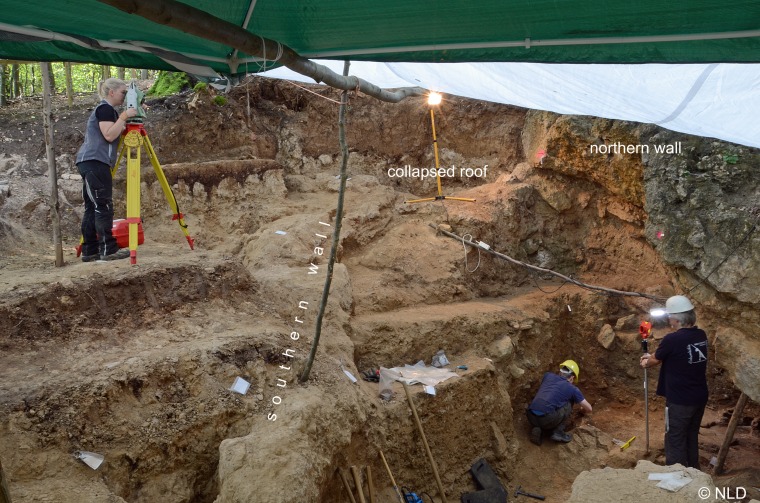 The former cave entrance where the engraved item was recovered. The item was found about 1 meter behind the person holding the staff. 