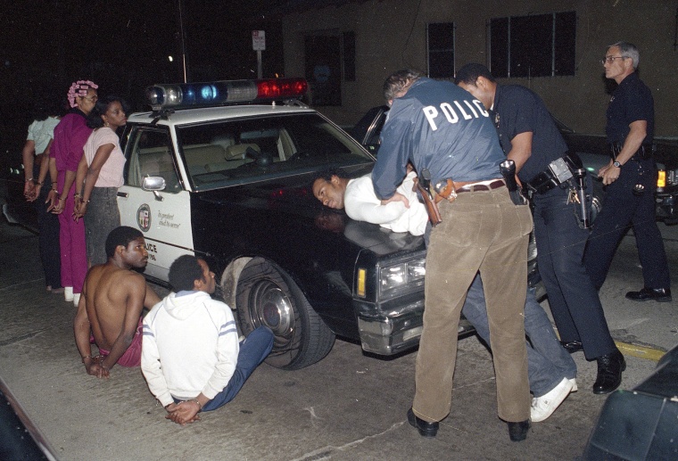 Los Angeles police officers search one of seven people arrested for selling narcotics in the south-central area of Los Angeles, as more than 1,000 police officers raided gang strongholds to attack on drug dealing and street violence in the nation's second largest city on April 9, 1988.