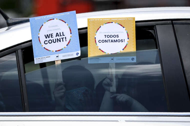Two young children hold signs through the car window that make reference to the 2020 U.S. Census, at an outreach event in Dallas on 25, 2020.