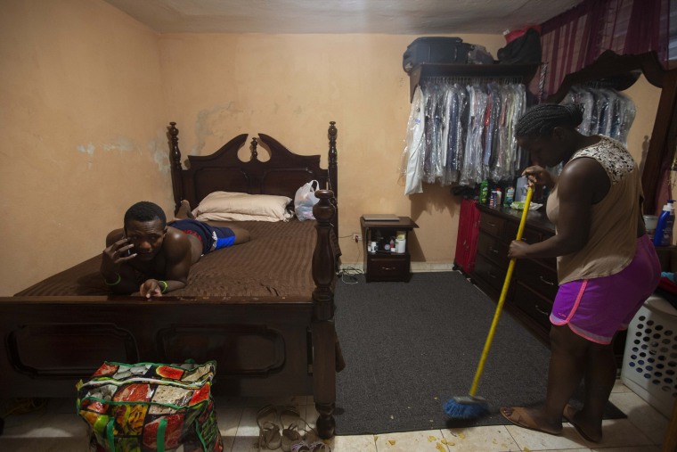 Jhon Celestin yace en una cama mientras su esposa Delta De Leon barre el piso en la casa de un familiar donde se hospedan en Puerto Príncipe, Haití, el jueves 23 de septiembre de 2021.