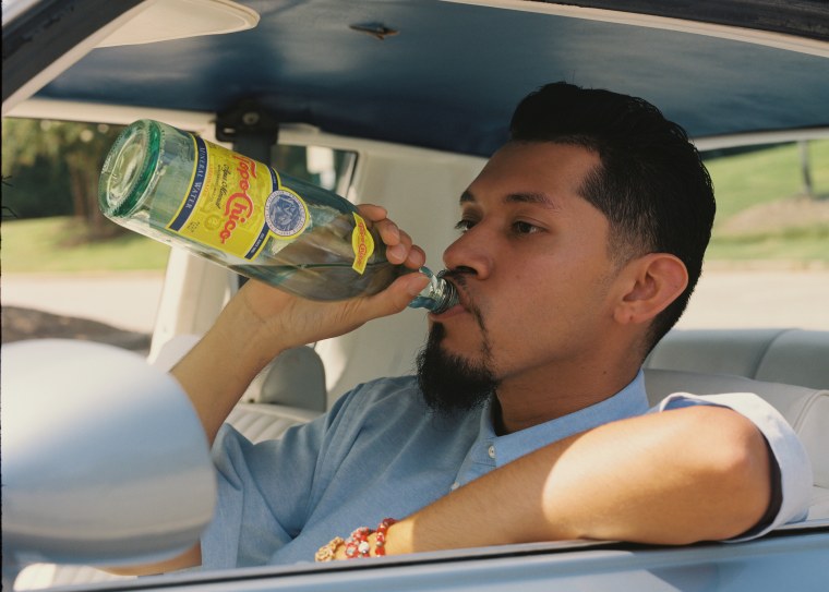 Corona se relaja en su auto, bebiendo una botella de agua mineral Topo Chico de México.