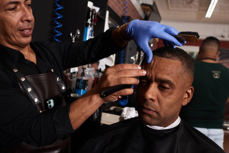 Rafael 'Lilo' Almonte, propietario de la barbería La Fama, cortando el pelo y charlando sobre la participación en la comunidad que ha llevado a cabo recientemente. Cliente: Raynel Bayne.