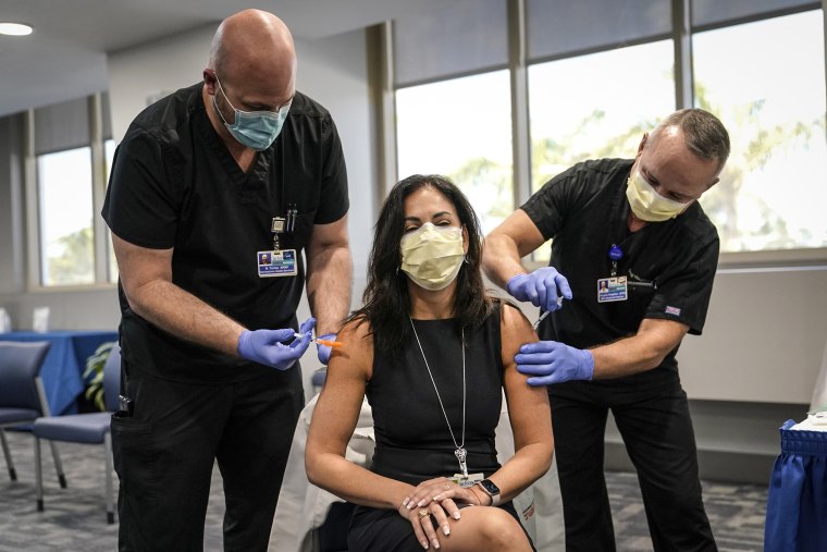 Image: Dr. Lilian Abbo, center, receives a flu vaccine from Nicholas Torres, left, and a Pfizer COVID-19 booster shot from Douglas Houghton, right, at Jackson Memorial Hospital on Oct. 5, 2021, in Miami.