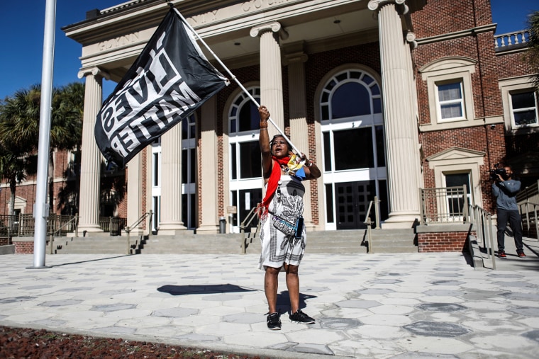 A woman waves a Black Lives Matter flag outside the Glynn County Courthouse, where jury selection in Ahmaud Arbery's murder trial is underway, in Brunswick, Ga., on Oct. 19, 2021.