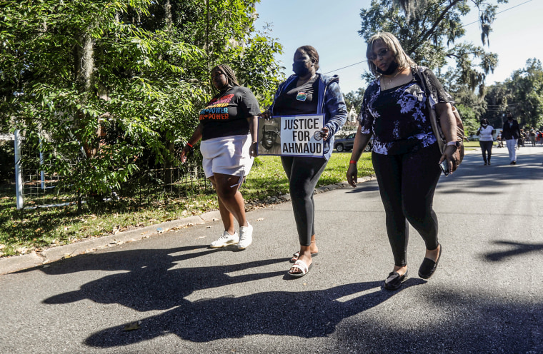 A woman holds a placard as people visit Satilla Shores neighborhood, where Ahmaud Arbery was killed, as the jury selection continues in Arbery's murder trial, in Brunswick, Ga., on Oct. 19, 2021.