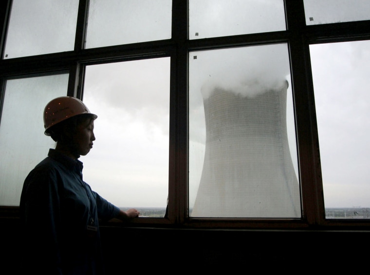 A worker looks out a window at a cooling tower at the Datang