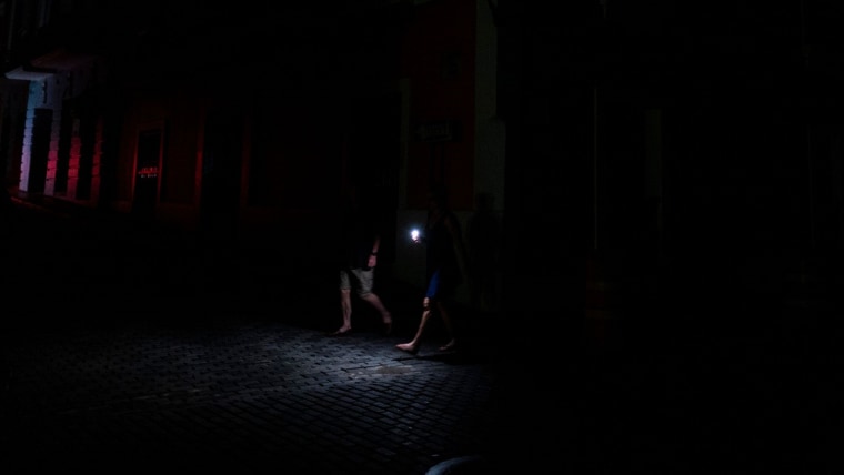 Dos personas caminan a oscuras iluminados solo por una linterna de celular en las calles de San Juan durante un apagón registrado en junio de 2021.